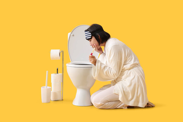 Jeune femme malade avec test de grossesse près du bol de toilette sur fond jaune - Photo, image