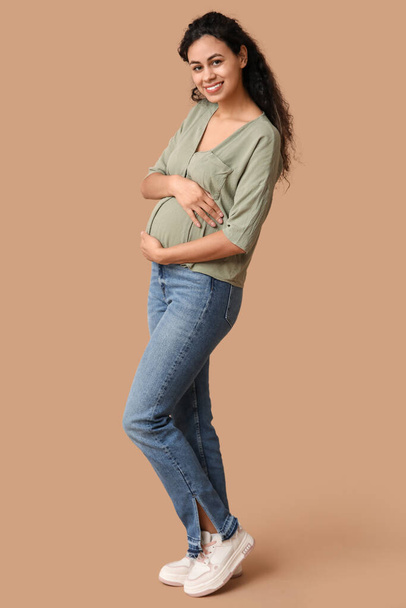 Ευτυχισμένη νεαρή έγκυος Αφρο-Αμερικανίδα σε καφέ φόντο - Φωτογραφία, εικόνα