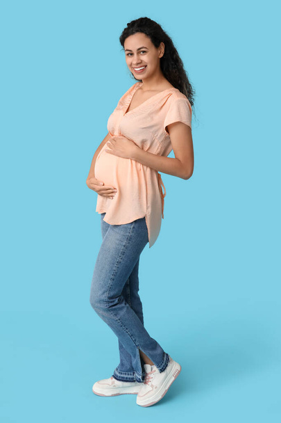 Mavi arka planda mutlu, hamile, Afro-Amerikan kadın. - Fotoğraf, Görsel