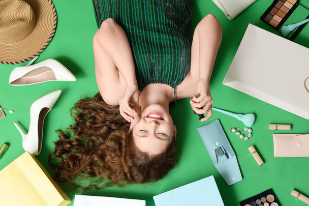 Bella giovane donna con cosmetici decorativi, tacchi alti alla moda e borse della spesa su sfondo verde - Foto, immagini
