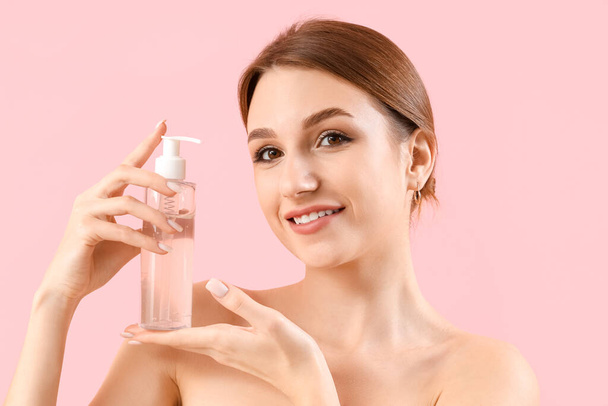 Belle jeune femme avec bouteille de produit cosmétique sur fond rose - Photo, image