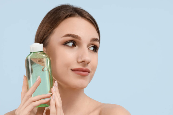 Mooie jonge vrouw met fles micellair water op blauwe achtergrond - Foto, afbeelding