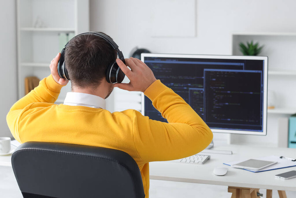 Programmeur masculin dans les écouteurs travaillant avec l'ordinateur dans le bureau, vue arrière - Photo, image