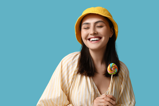 Ευτυχισμένη νεαρή γυναίκα με γλυκό γλειφιτζούρι σε μπλε φόντο - Φωτογραφία, εικόνα