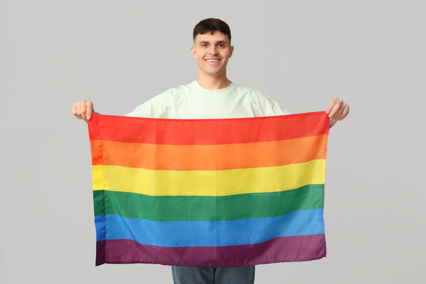 Przystojny młody szczęśliwy mężczyzna z flagą LGBT na szarym tle - Zdjęcie, obraz