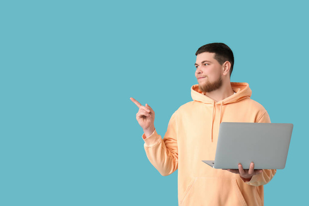 Mladý vousatý muž s notebookem ukazuje na něco na modrém pozadí - Fotografie, Obrázek