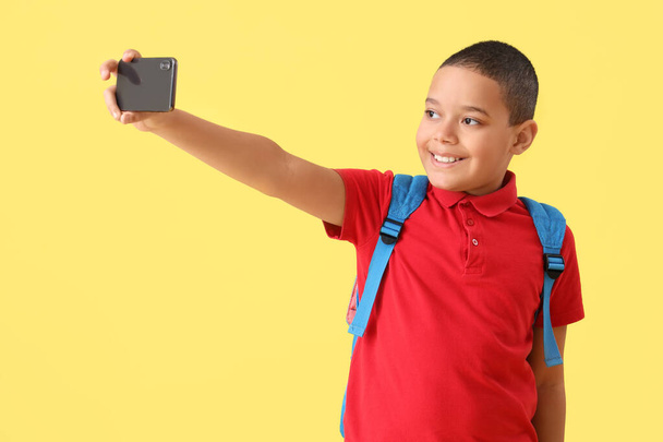 Felice piccolo scolaretto afroamericano con zaino scattare selfie su sfondo giallo - Foto, immagini