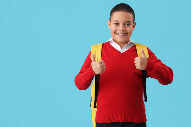 Šťastný malý africko-americký školák s batohem ukazujícím palec nahoru gesto na modrém pozadí - Fotografie, Obrázek