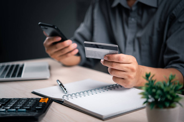 Man with credit card and smartphone finalizes a transaction, with a calculator and notepad nearby. online payment transaction e commerce shopping internet finance banking business concept. - Photo, Image