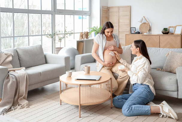 Giovane donna incinta con moglie che applica la crema sulla pancia a casa - Foto, immagini