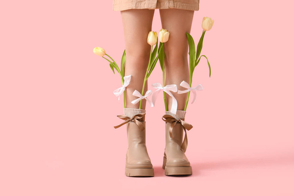 Stylowa młoda kobieta z kokardkami i tulipanami w butach na różowym tle, zbliżenie - Zdjęcie, obraz