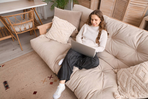 Молодая женщина с ноутбуком на мягком диване дома - Фото, изображение