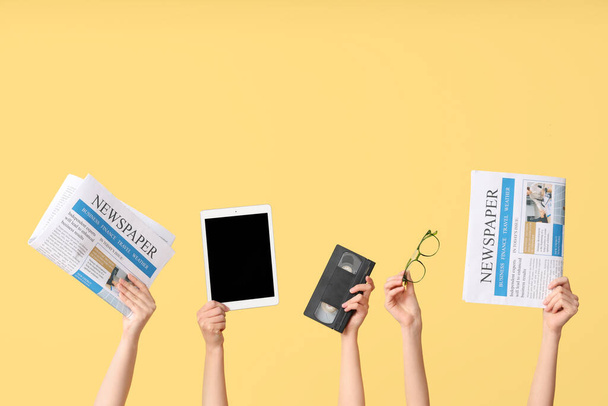 Manos femeninas con periódicos, tablet computer, video cassette y anteojos sobre fondo amarillo - Foto, imagen