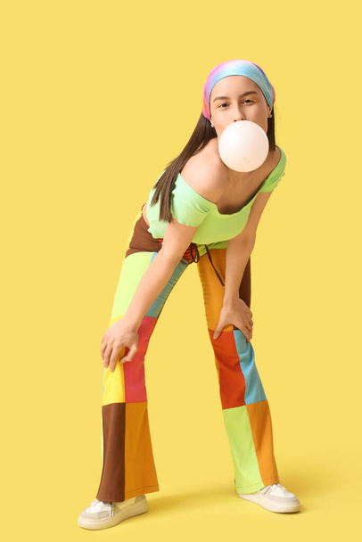 Schöne junge modische Frau bläst Kaugummi auf gelbem Hintergrund - Foto, Bild