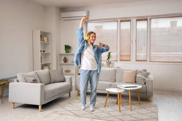 Fiatal nő a fejhallgatóban táncol a világos nappaliban - Fotó, kép