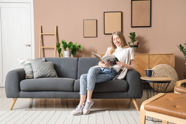 Молодая красивая женщина читает журнал на диване в стильной гостиной - Фото, изображение