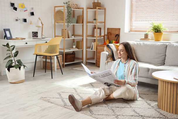 Mujer bonita joven leyendo el periódico en el suelo en la sala de estar de luz - Foto, Imagen