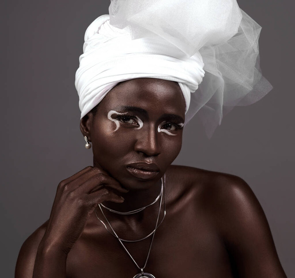 Portrait, wrap and black woman with makeup, beauty and confidence in studio on grey background. Face, glow and proud African model with traditional outfit, eyeshadow cosmetics or creative necklace. - Photo, Image