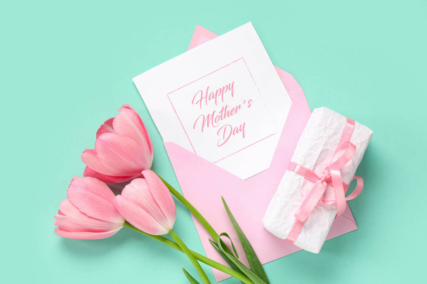 Pozdrav s textem Šťastný den matek, krásné růžové tulipány a dárková krabička na tyrkysovém pozadí - Fotografie, Obrázek