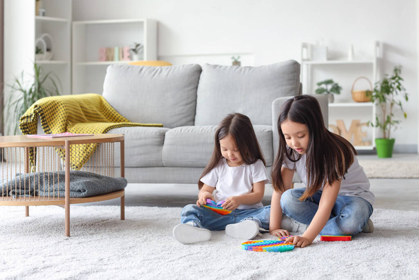schattig klein aziatisch gelukkig zussen spelen met verschillende pop het fidget speelgoed op de vloer thuis - Foto, afbeelding