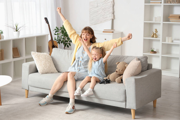 Kindermädchen mit kleinem Mädchen spielt Videospiel auf dem Sofa zu Hause - Foto, Bild