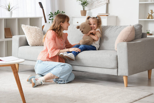 Nanny and little girl with toy bear on sofa at home - Photo, Image