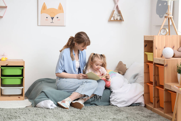 Nanny with little girl reading book in bedroom - Photo, Image