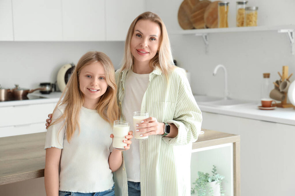 Gelukkig dochter en haar moeder met kopjes melk in de keuken thuis - Foto, afbeelding