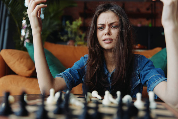 Frau in Not sitzt mit den Händen auf dem Kopf an einem Tisch und betrachtet ein Schachbrett vor sich - Foto, Bild