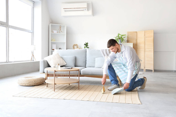 Junger bärtiger Mann fegt Teppich zu Hause - Foto, Bild