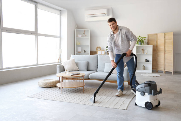 Giovane uomo barbuto pulizia tappeto a casa - Foto, immagini