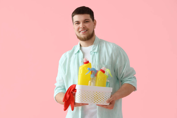Young bearded man with bucket of cleaning supplies on pink background - Photo, Image