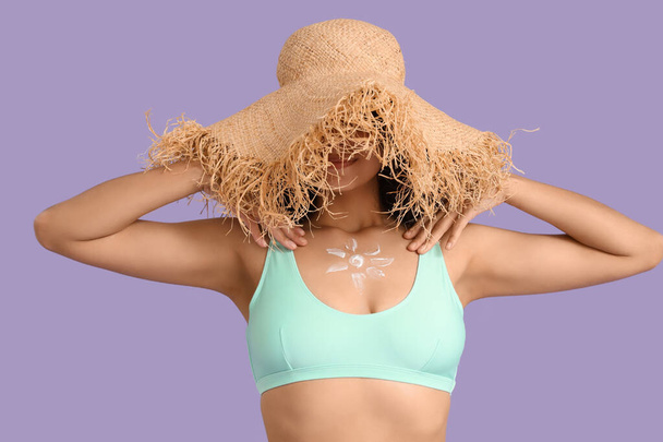 Молода афроамериканка в солом'яному капелюсі з сонцем з сонцезахисного крему на бузковому фоні - Фото, зображення
