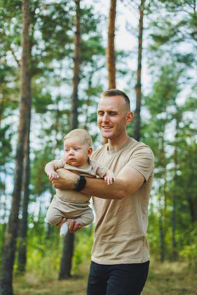 Un giovane padre tiene il suo piccolo figlio tra le braccia mentre è in piedi nel parco. Papà sta giocando con suo figlio - Foto, immagini