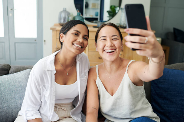 Happy woman, friends and photography with selfie on sofa for memory, bonding or moment together at home. Female person or young people with smile for picture or capture on mobile smartphone at house. - Photo, Image