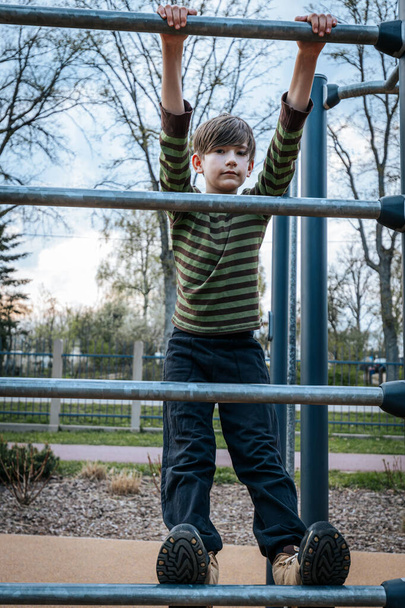 child rested in the childrens playground. The boy was hanging on the bars. Smiling happy child - Photo, Image