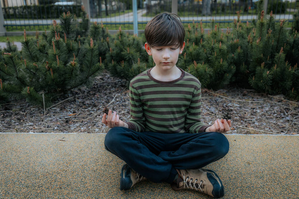 Мальчик сидит и медитирует. Ребенок отдыхает и медитирует. Улыбающийся счастливый ребенок - Фото, изображение