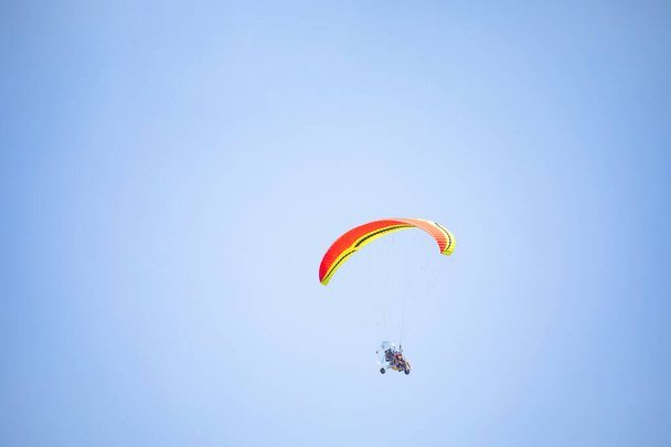 Motorisierter Tandemflug mit Fallschirm, zweisitziger motorisierter Gleitschirm mit Rädern. Unerkennbare Menschen hoch oben am Himmel auf einem motorisierten Trike mit Flügel - Foto, Bild