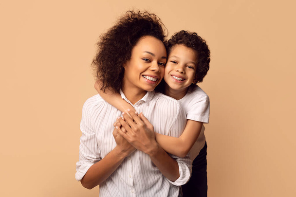 Una gioiosa madre afroamericana stringe il figlio in un tenero abbraccio, entrambi con camicie bianche, mostrando l'affettuoso legame tra genitore e figlio. - Foto, immagini