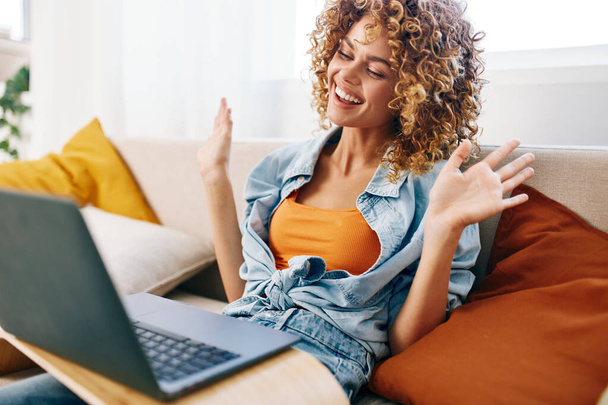 Усміхнена жінка працює на ноутбуці в затишній вітальні, насолоджуючись позаштатною роботою - Фото, зображення