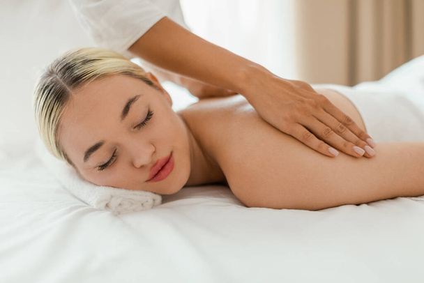 Una mujer se acuesta boca abajo en una mesa de masaje en un entorno de spa sereno, mientras que un terapeuta de masaje realiza un masaje de espalda en ella. Las manos de los terapeutas son visibles al aplicar presión y amasar - Foto, Imagen