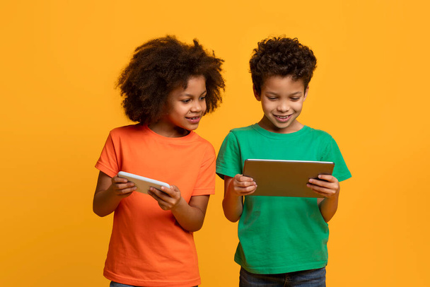 Deux jeunes enfants afro-américains, un garçon et une fille, se tiennent côte à côte, absorbés dans l'écran d'une tablette. Ils semblent concentrés et curieux, explorant ensemble le monde numérique - Photo, image
