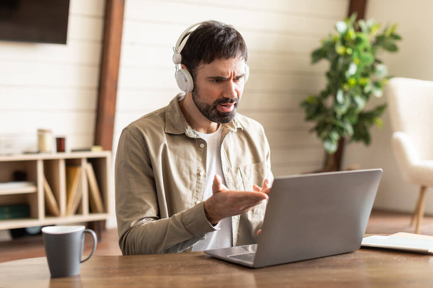 Ein Mann sitzt mit Kopfhörern auf einem Laptop-Bildschirm. Er scheint engagiert und aufmerksam auf die Informationen, die auf dem Computer angezeigt werden, haben Videoanrufe - Foto, Bild