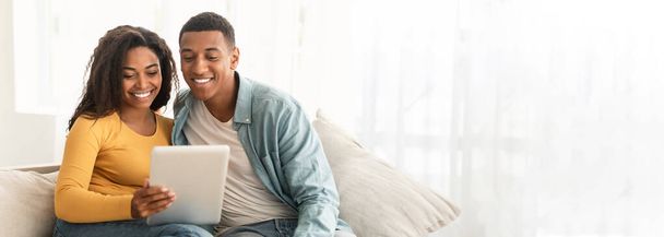 Contenuto Coppia afroamericana che utilizza un tablet su un divano, offrendo un'immagine accogliente con spazio web-banner copia - Foto, immagini