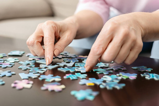 Cropped of woman carefully placing a puzzle piece on a wooden table. The puzzle is partially completed, showing a colorful image of a landscape - Photo, Image