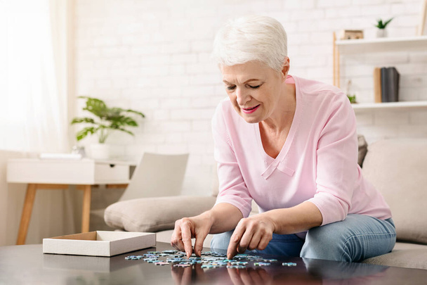 Activiteit kan de hersenfunctie verbeteren. Oudere vrouw zittend aan tafel en sorteren puzzelstukjes, vrije ruimte - Foto, afbeelding