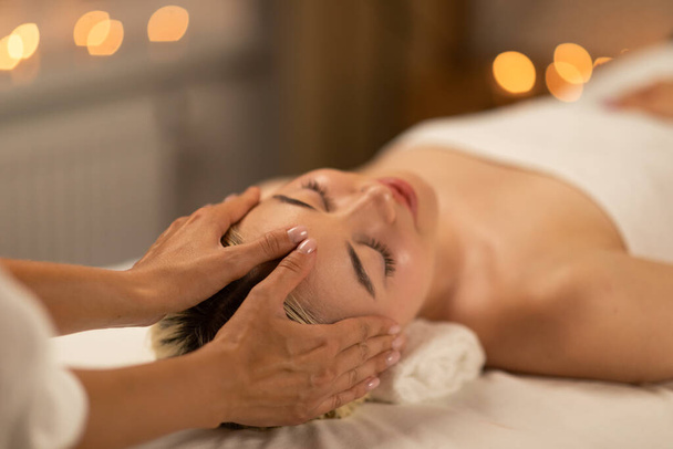 A calming scene at a spa with a young blonde woman receiving a delicate facial massage, showcasing her relaxed demeanor and comfort. - Photo, Image