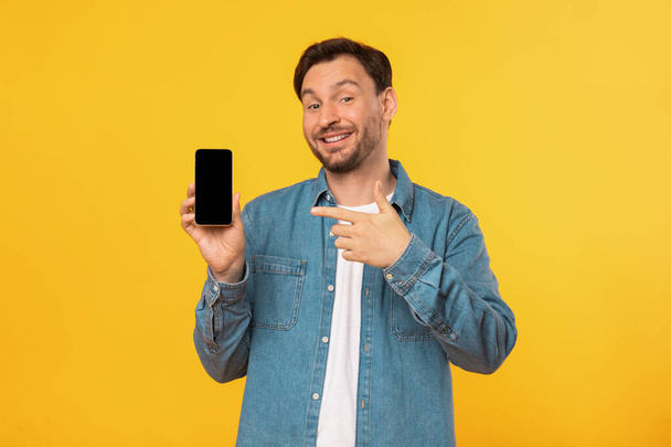 Un uomo che indossa una camicia blu tiene in mano un cellulare, guardando lo schermo con attenzione. Lo sfondo è neutro, consentendo allo spettatore di concentrarsi sul soggetto principale e l'azione nell'immagine. - Foto, immagini