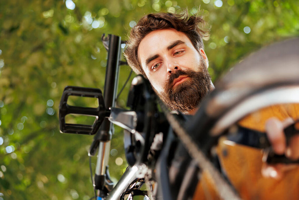 Активний біговий чоловік, який працює на зламаному велосипедному кільці з професійним обладнанням на домашньому подвір'ї. Спортивний чоловік обслуговує велосипед на вулиці для літнього дозвілля їзда на велосипеді. - Фото, зображення