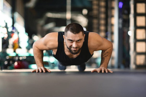 Egy férfi fekvőtámaszt ad a tornaterem padlóján. Edzőruhát visel, és a gyakorlatára koncentrál, bizonyítva az erejét és elszántságát az edzésben.. - Fotó, kép
